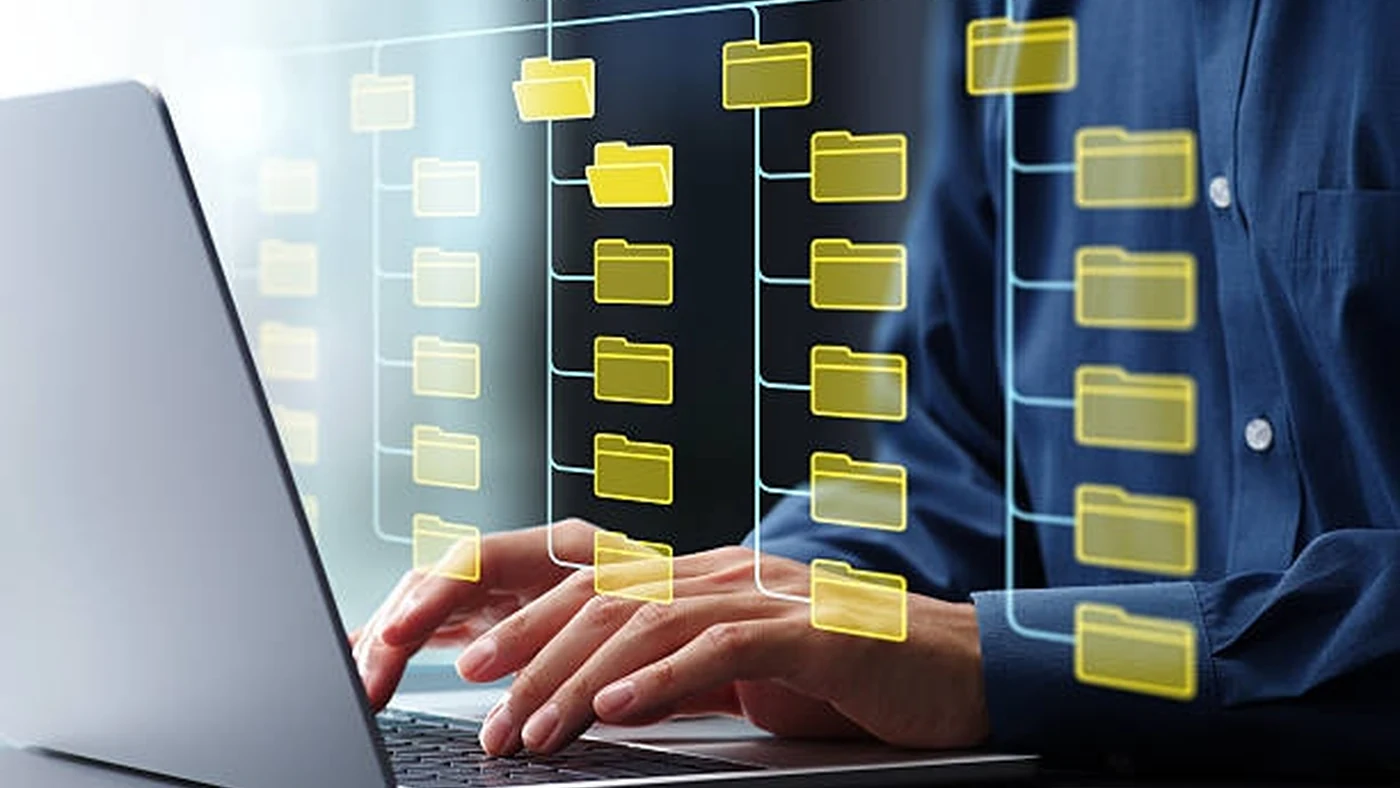 Hands at a laptop keyboard arrange a hierarchical structure of connected folders floating above the screen.