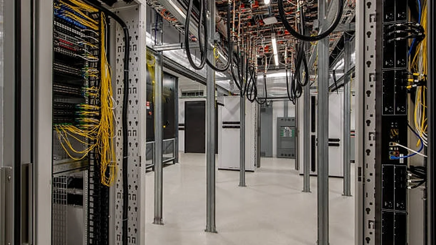 Two workers in high-visibility vests beneath overhead cable tray runs in a new data center shell.