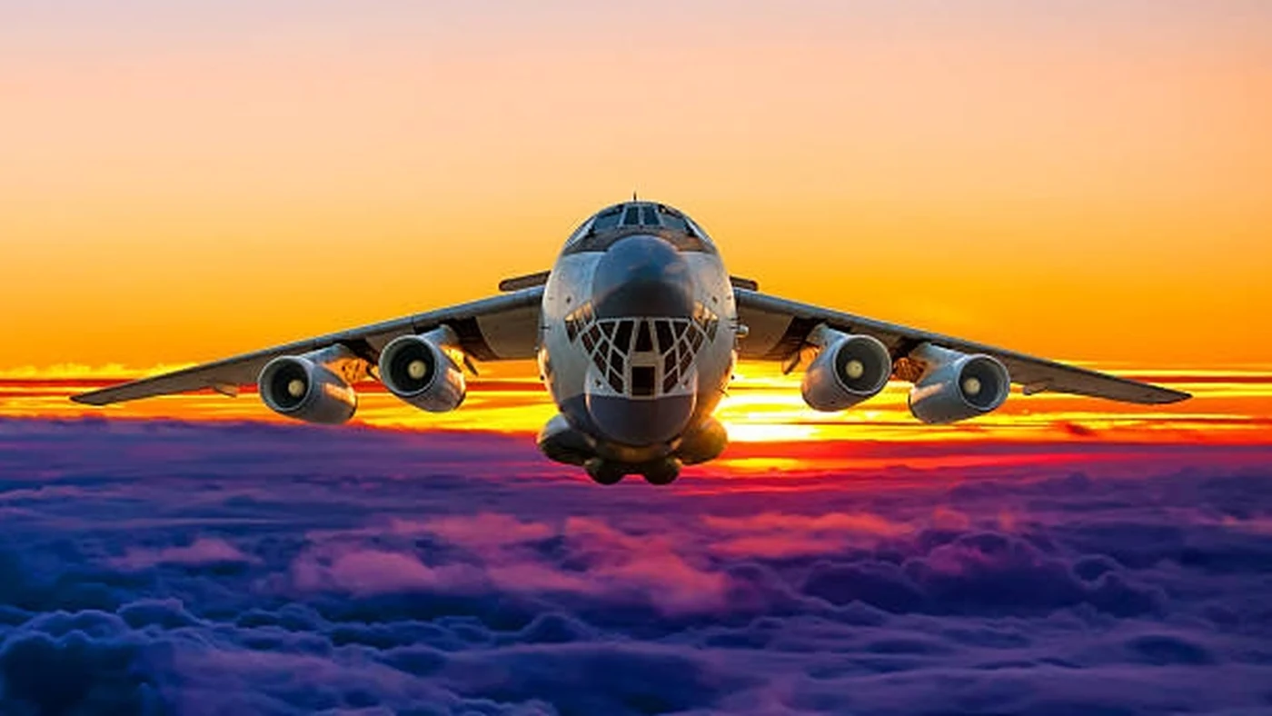 A large transport aircraft flies above the clouds at sunset with wings level and engines steady.